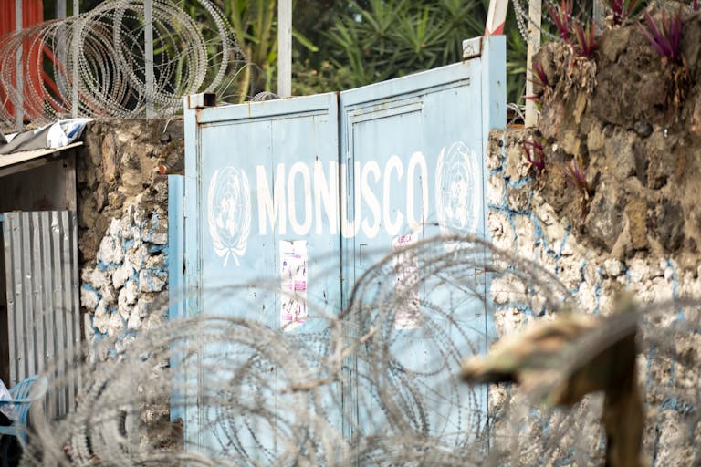 Barbed wire protecting the MONUSCO gate, surrounded by stone walls and plants.