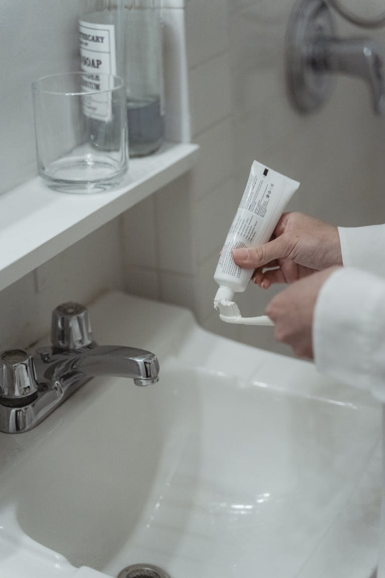 Close-up of a person applying toothpaste on a toothbrush in a clean, modern bathroom setting.