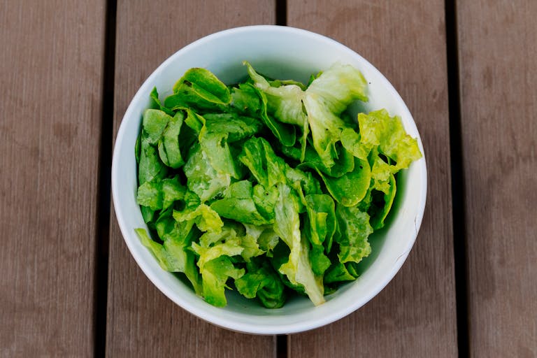Crisp green lettuce in a white bowl on a rustic wooden surface. Perfect for healthy eating.
