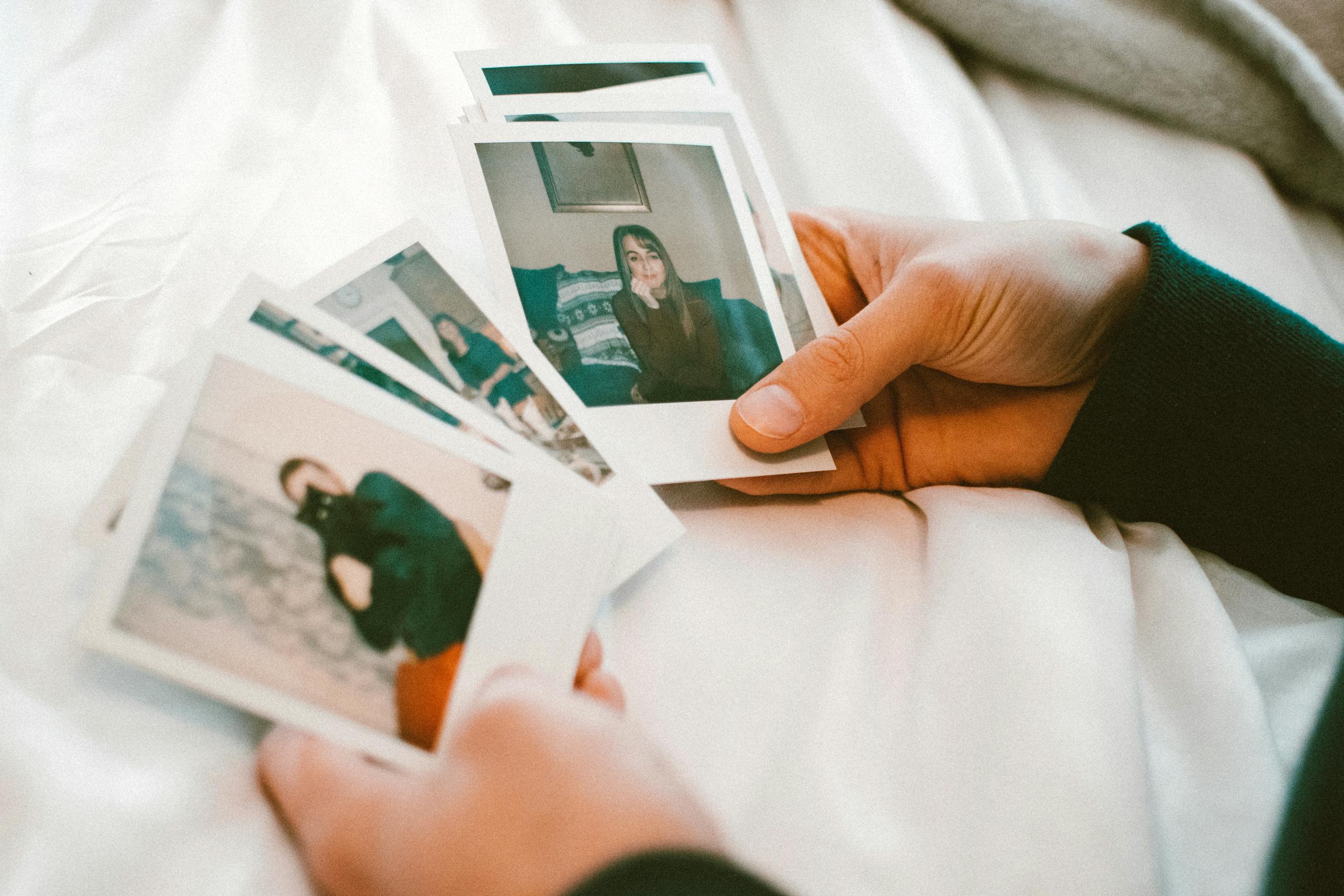 Hands gently holding a collection of printed photographs on a white bedspread.