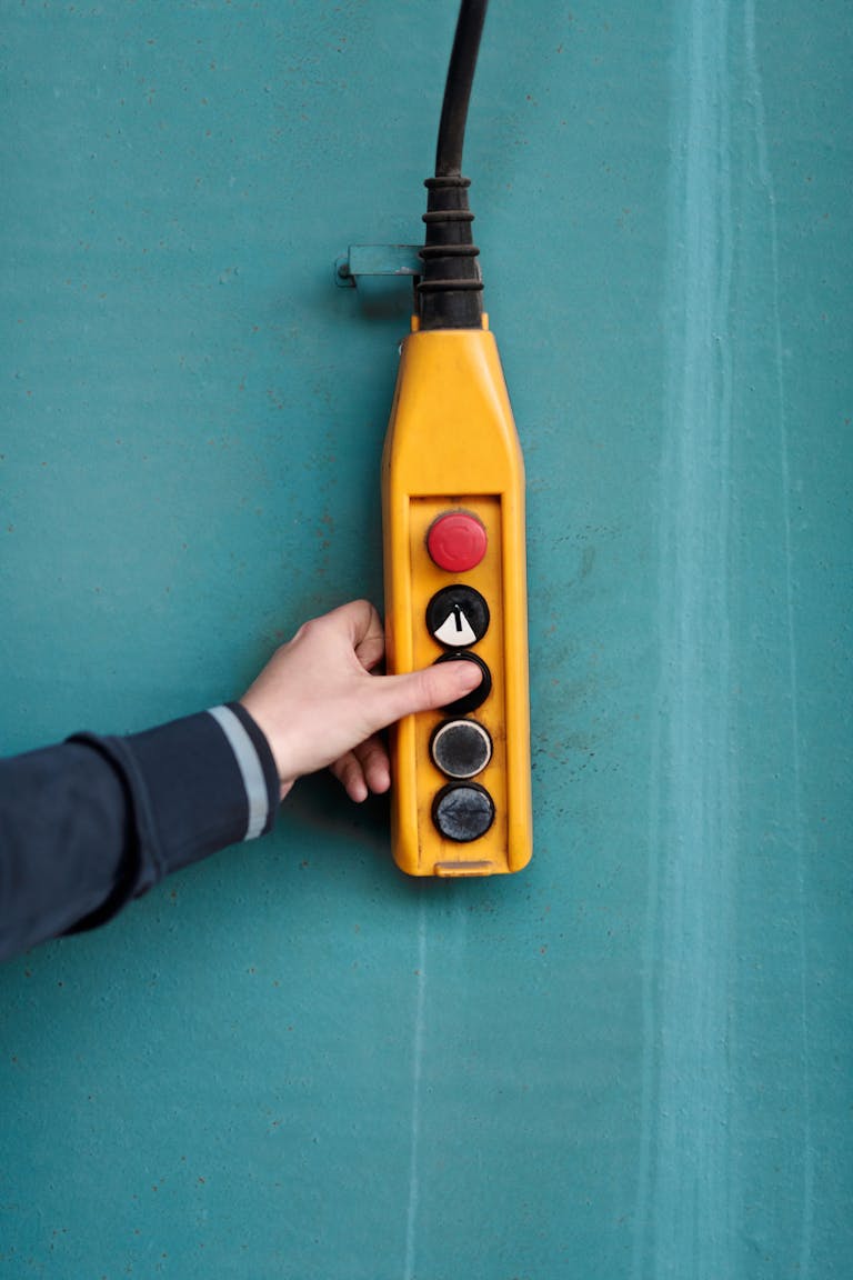 Close-up of a hand pressing a button on a yellow industrial control panel against a blue wall.
