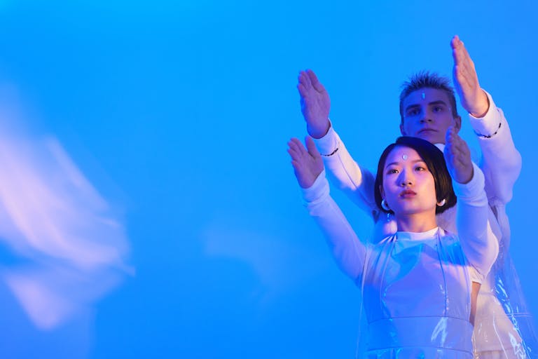 Futuristic portrait of man and woman posing with arms raised in blue lighting.