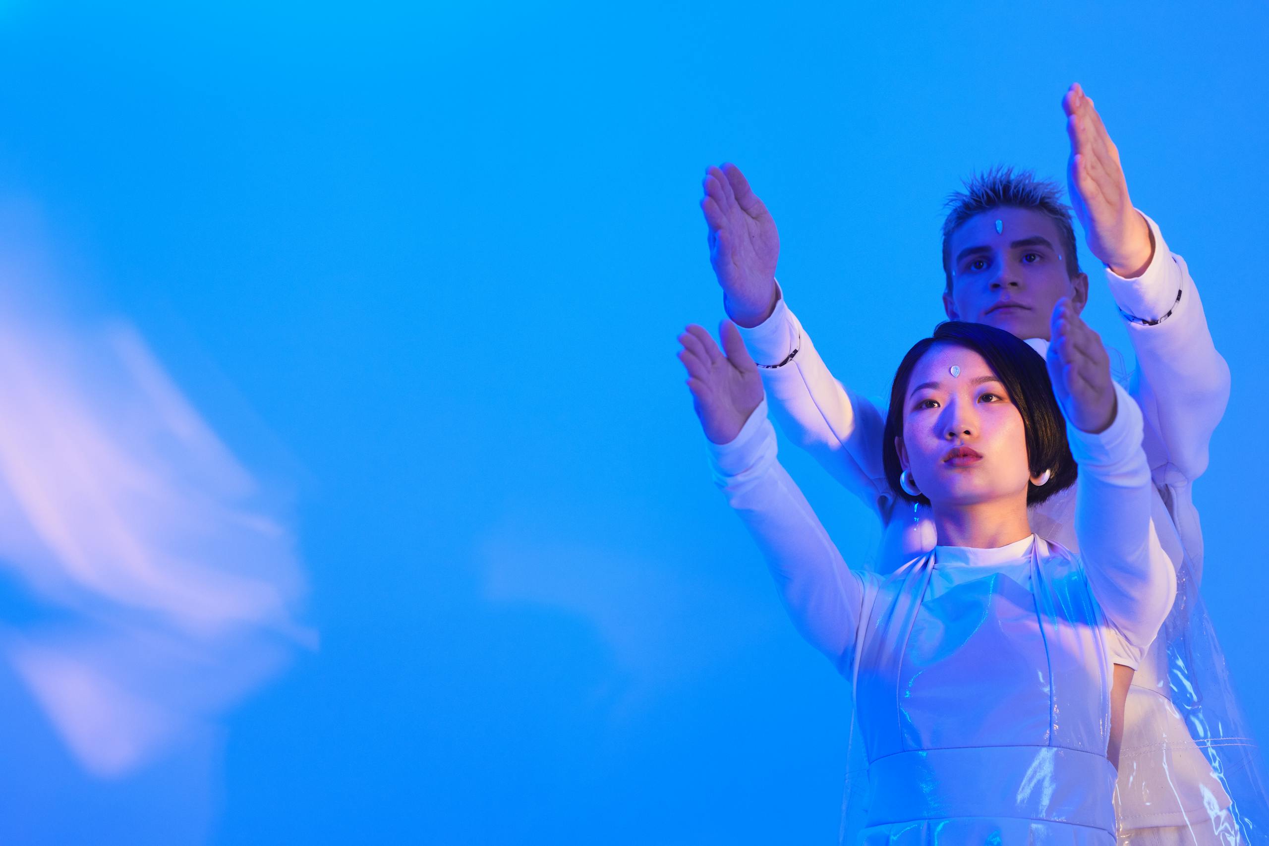 Futuristic portrait of man and woman posing with arms raised in blue lighting.