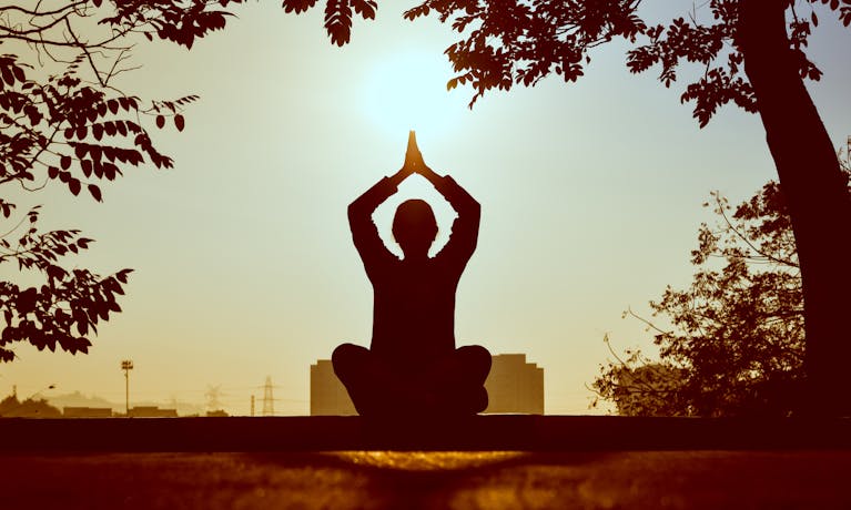 Silhouette of a person practicing yoga outdoors during sunrise, creating a calming atmosphere.