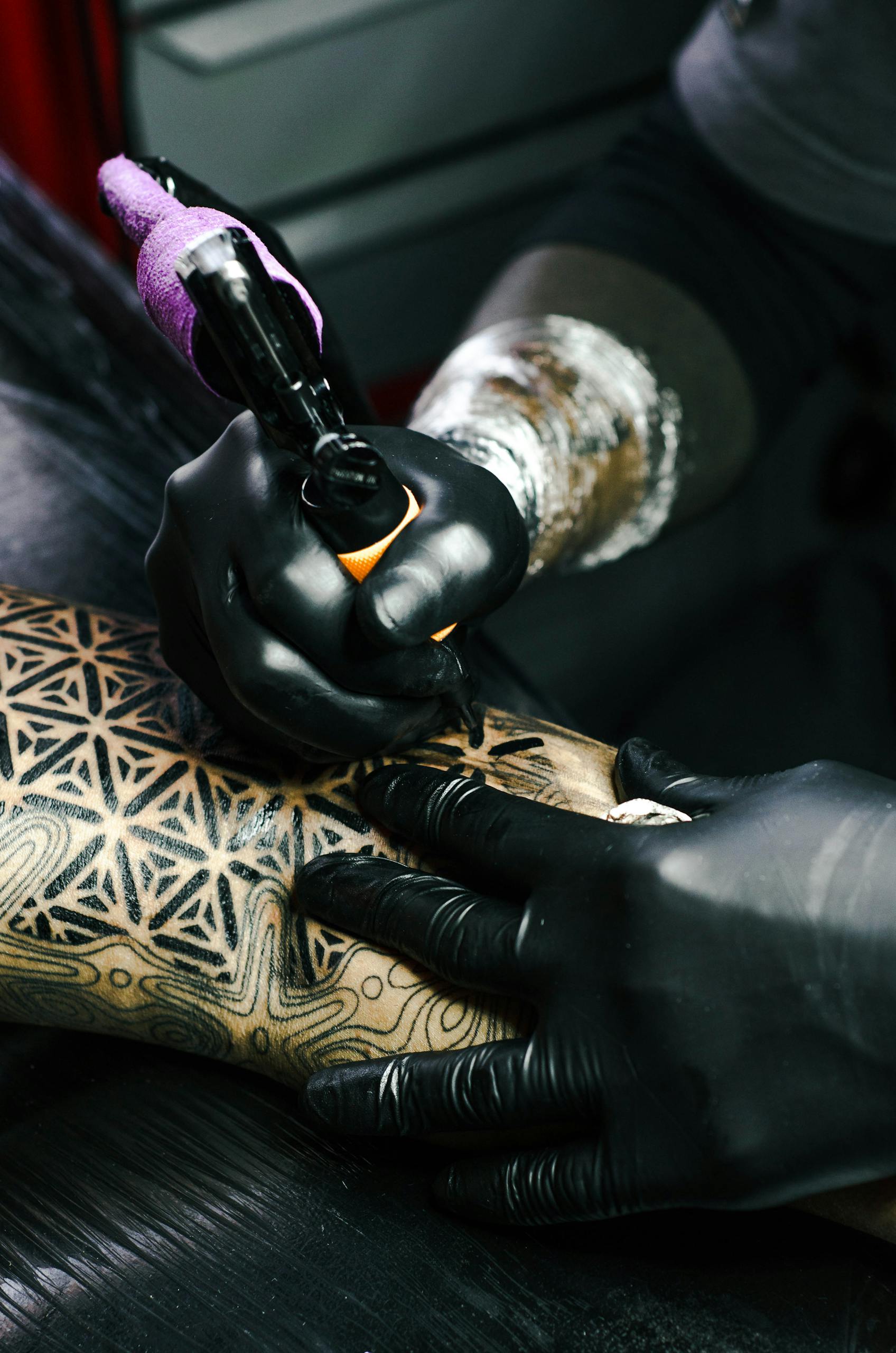 Tattoo artist working on intricate black and white design indoors.