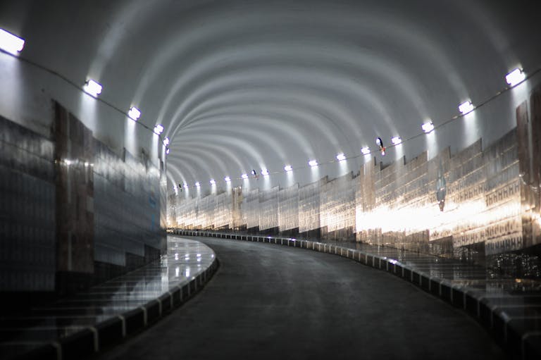 Curved road tunnel with reflective lights illuminating smooth walls in a mysterious setting.
